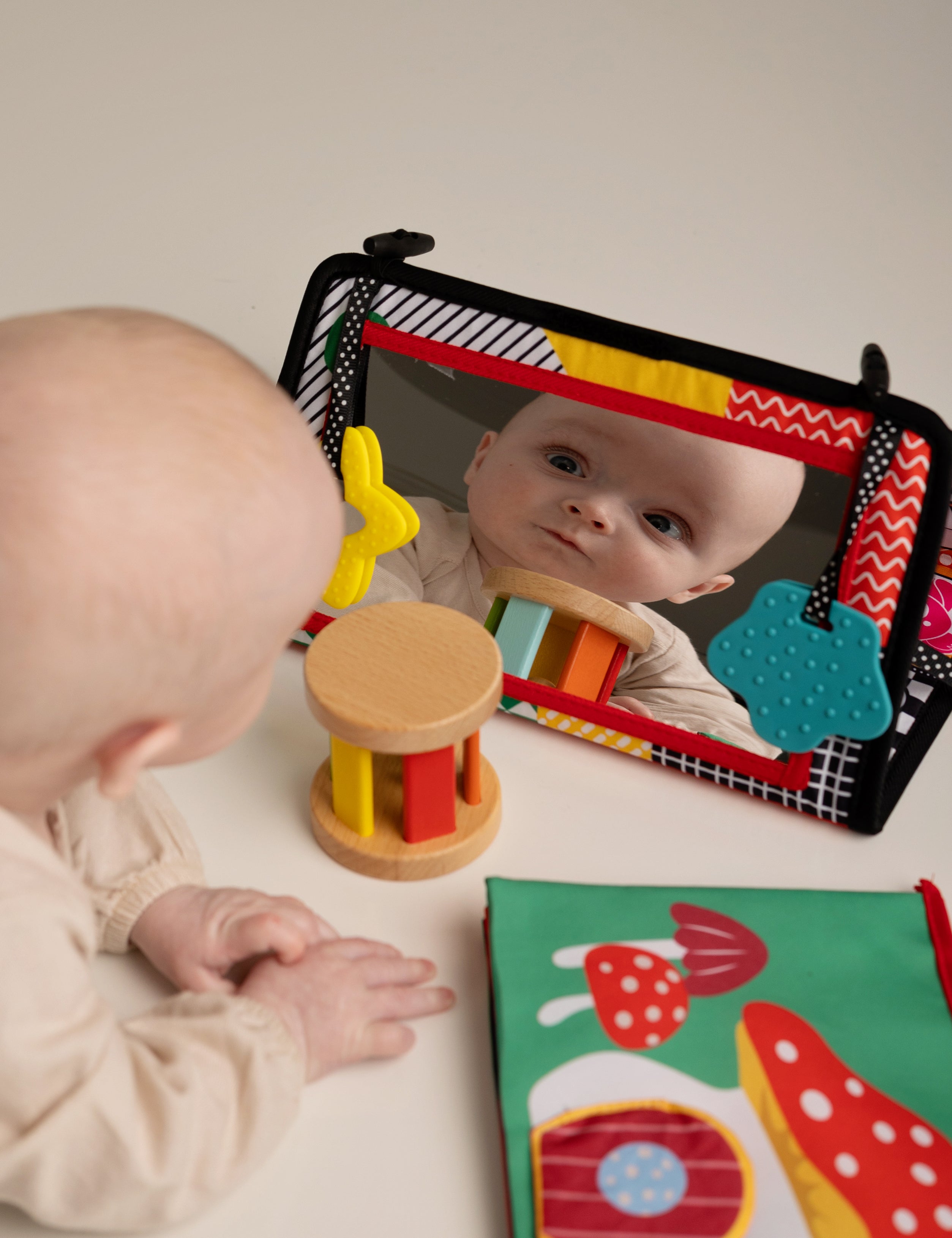 Baby interacting with a colorful toy and mirror on a white surface