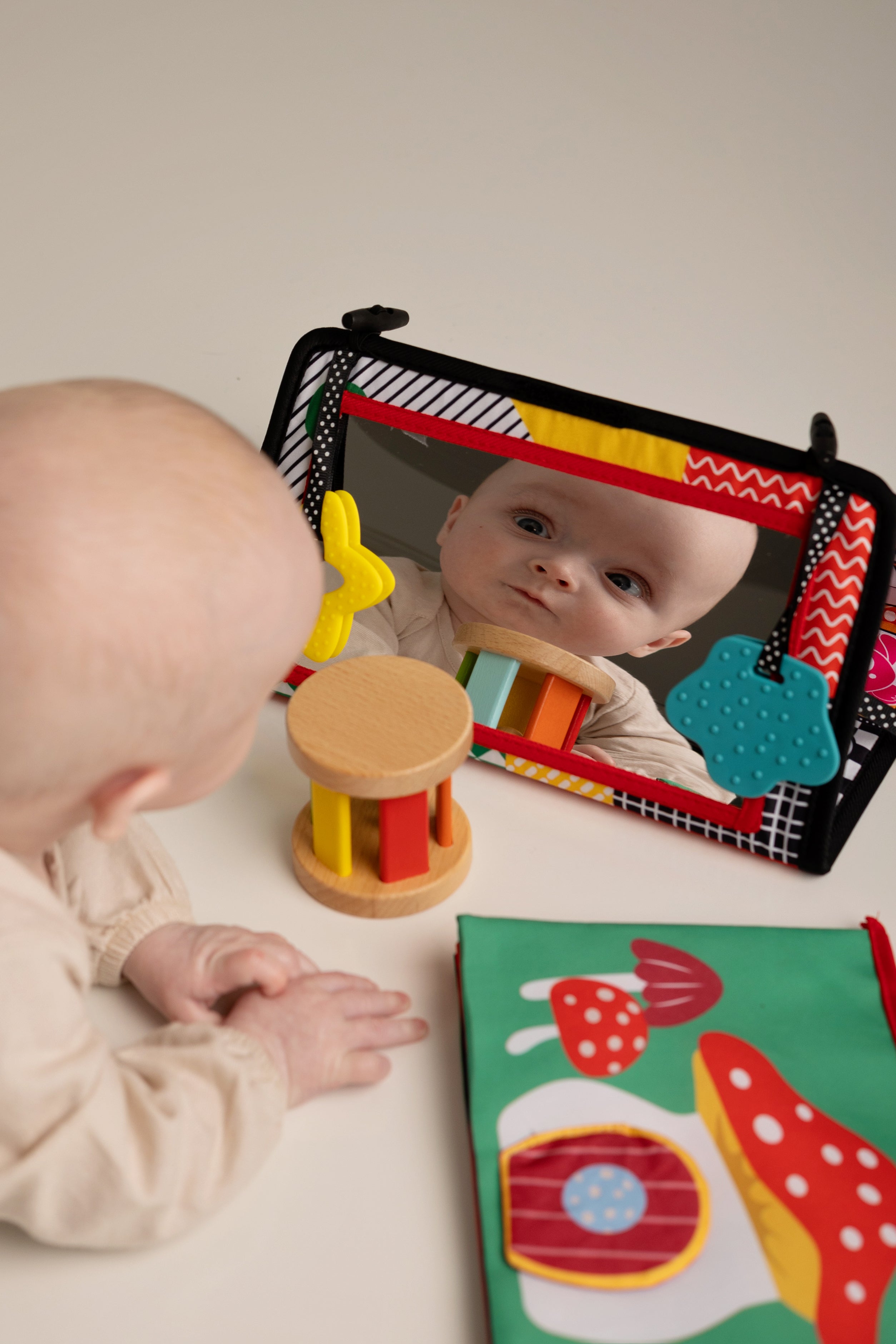 Baby interacting with a colorful toy and mirror on a white surface
