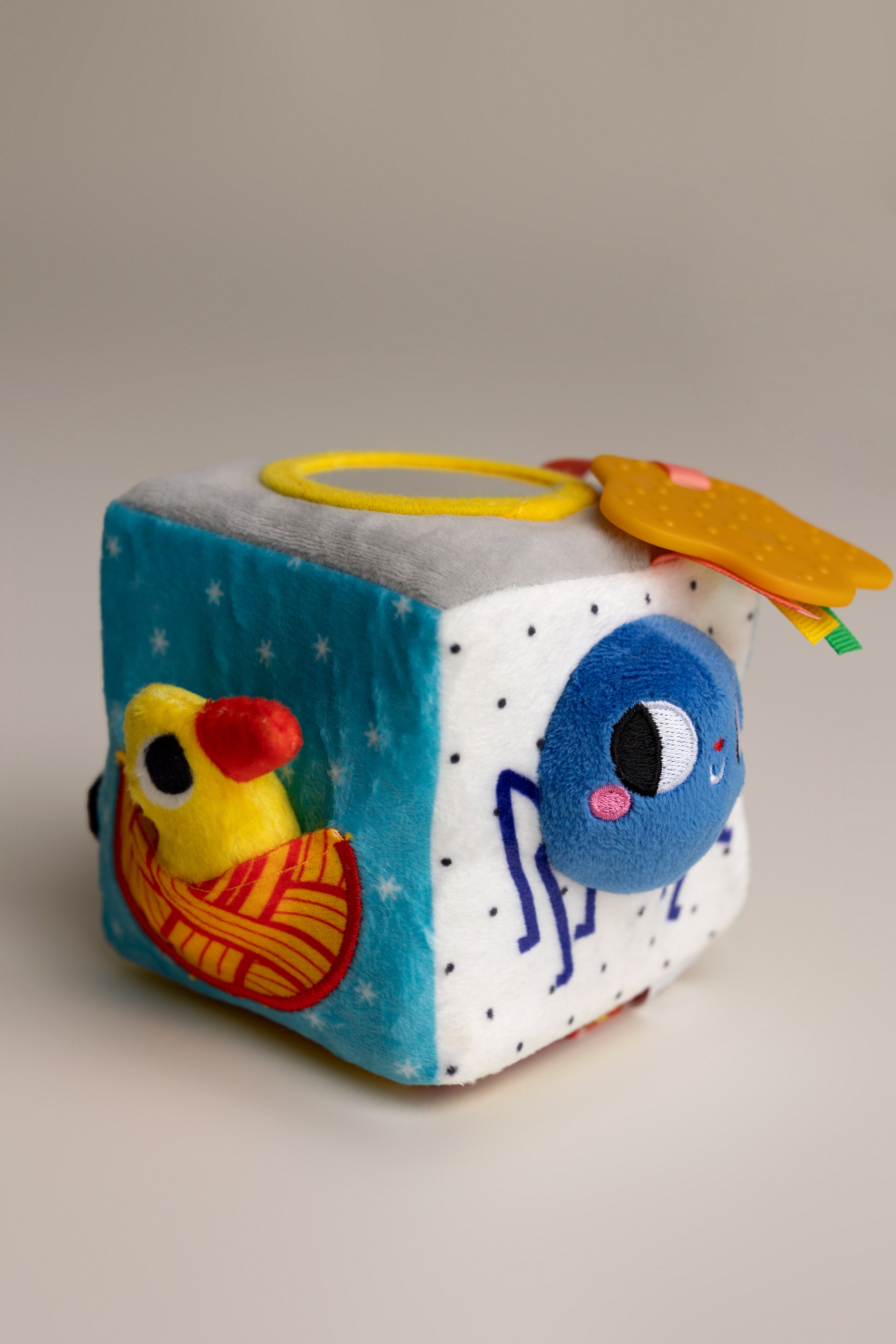 Colorful plush cube toy with cartoon characters on a neutral background