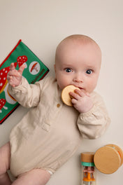 Baby holding a wooden toy with a book in the background
