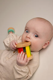 Baby playing with a colorful wooden toy against a plain background