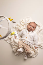 Newborn baby in a white outfit with a knitted blanket and toys on a light background