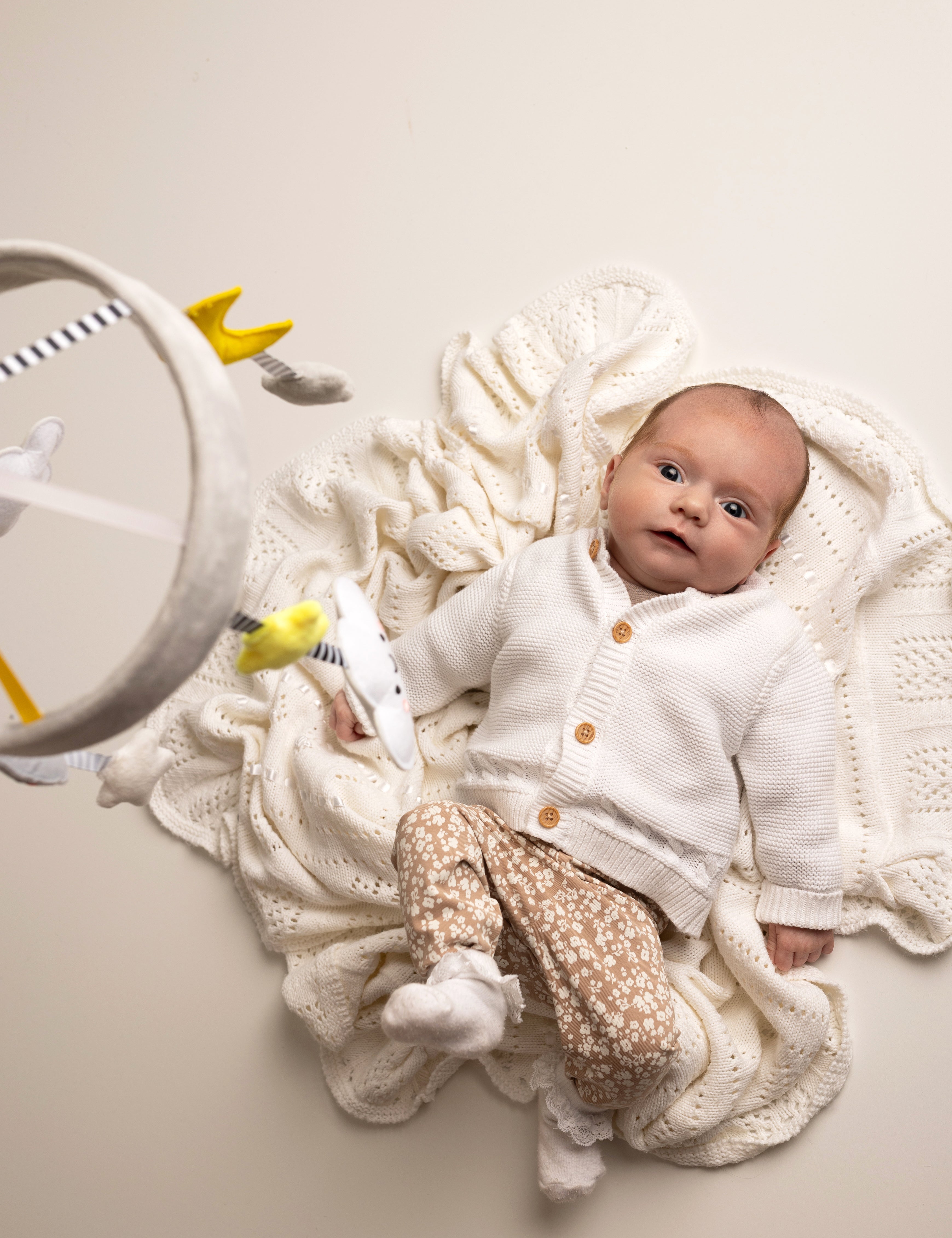 Newborn baby in a white outfit with a knitted blanket and toys on a light background