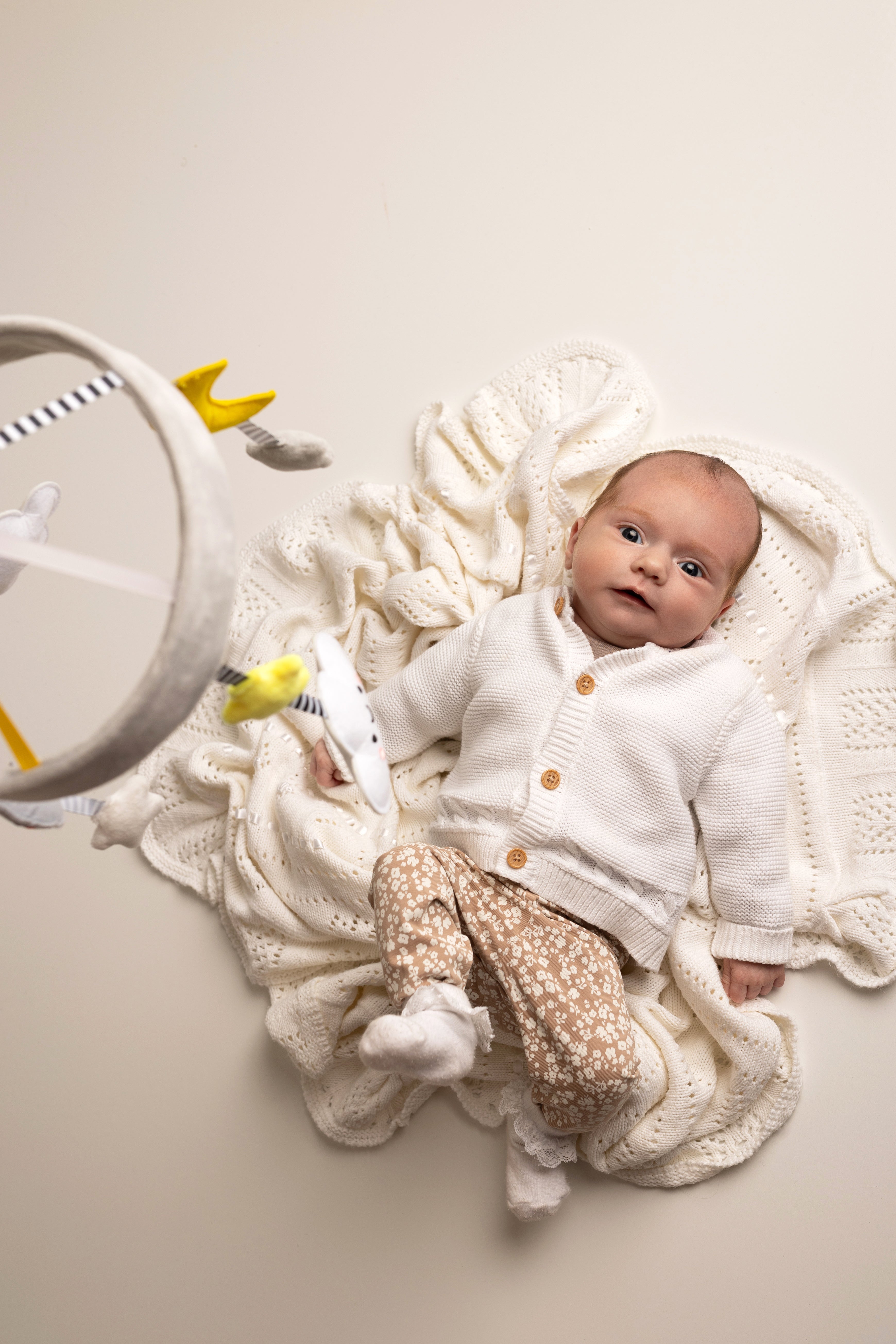 Newborn baby in a white outfit with a knitted blanket and toys on a light background