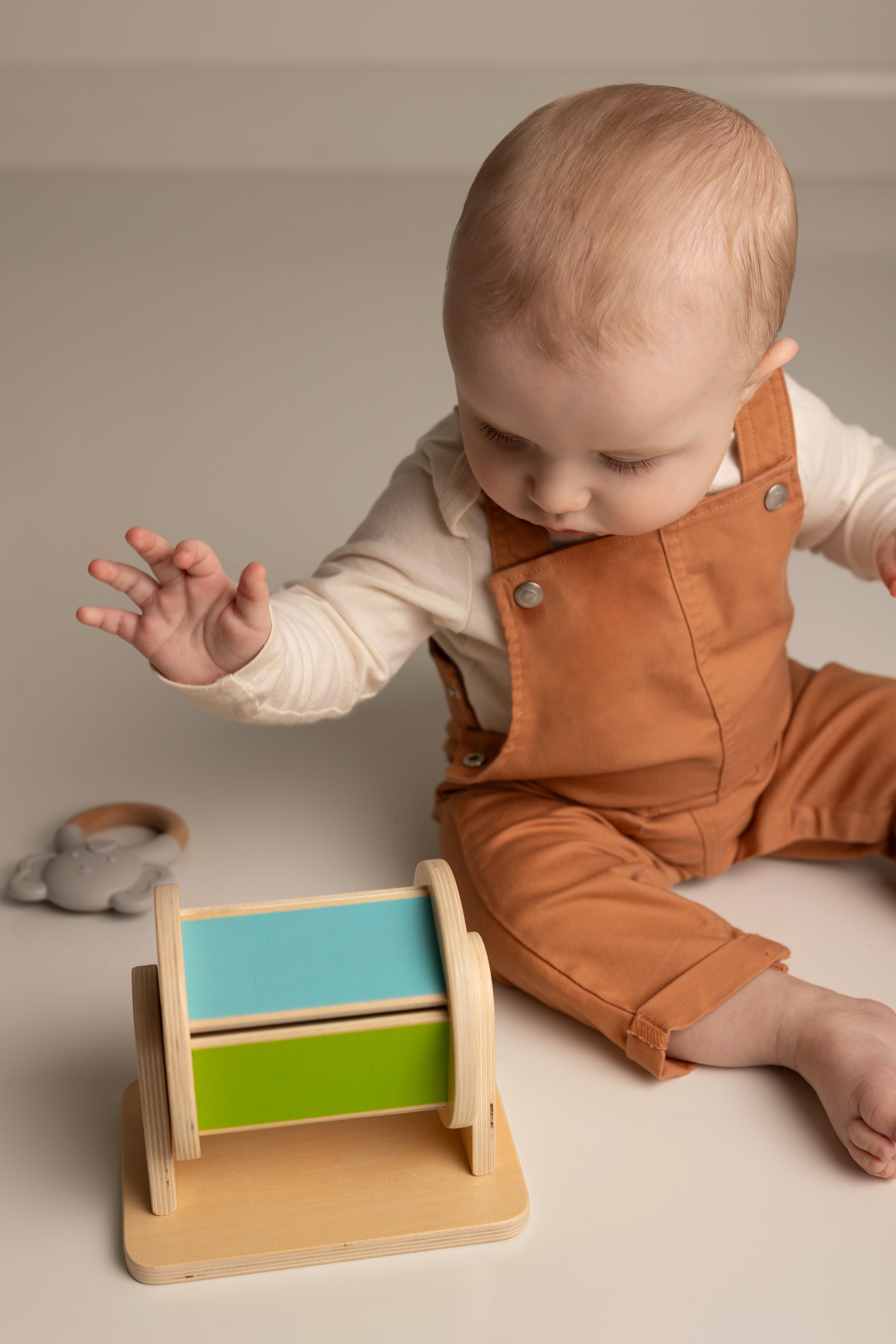 Baby playing with a wooden toy on a neutral background