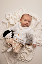 Baby in a white outfit with a black and white doll on a textured blanket