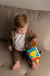 Child playing with a colorful soft cube on a beige couch