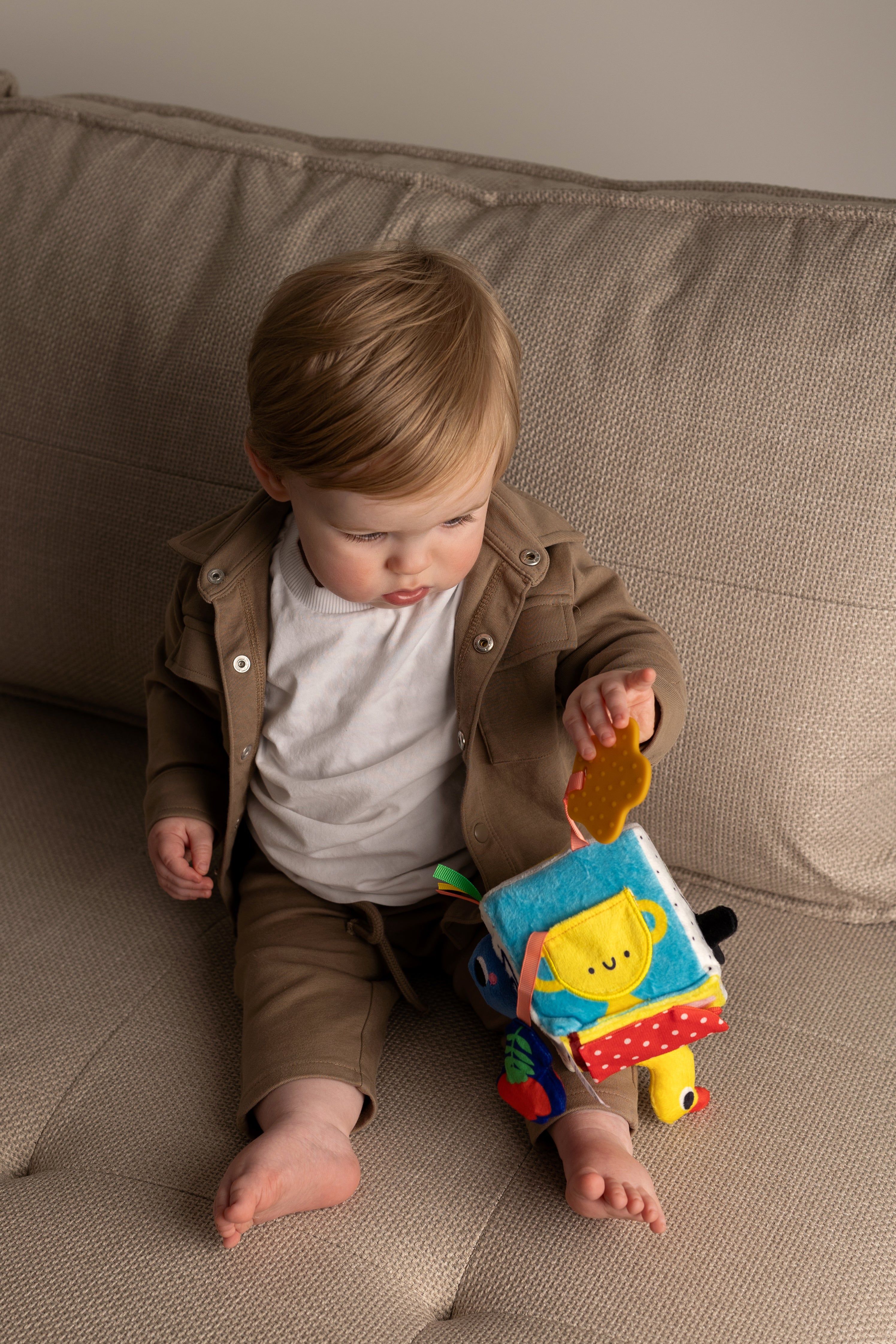 Child playing with a colorful soft cube on a beige couch