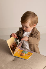 Child holding a book with a picture of a baby on a couch